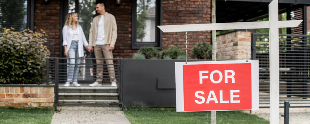 couple of home owners holding hands for sale sign in front yard